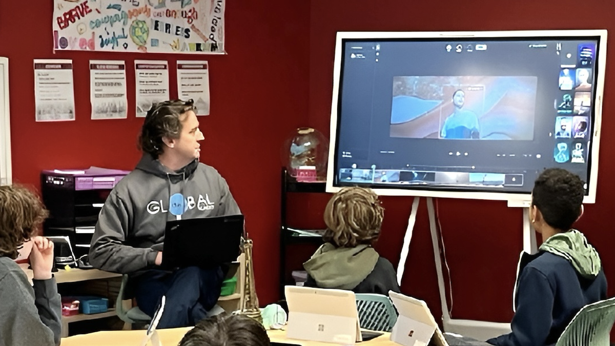 Juan M. Lavista Ferres is pictured holding a laptop while students watch a video about AI on a screen, linking education and technology.