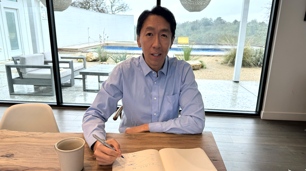 Andrew Ng is pictured writing in a notebook by a large window, with a garden and pool visible in the background.
