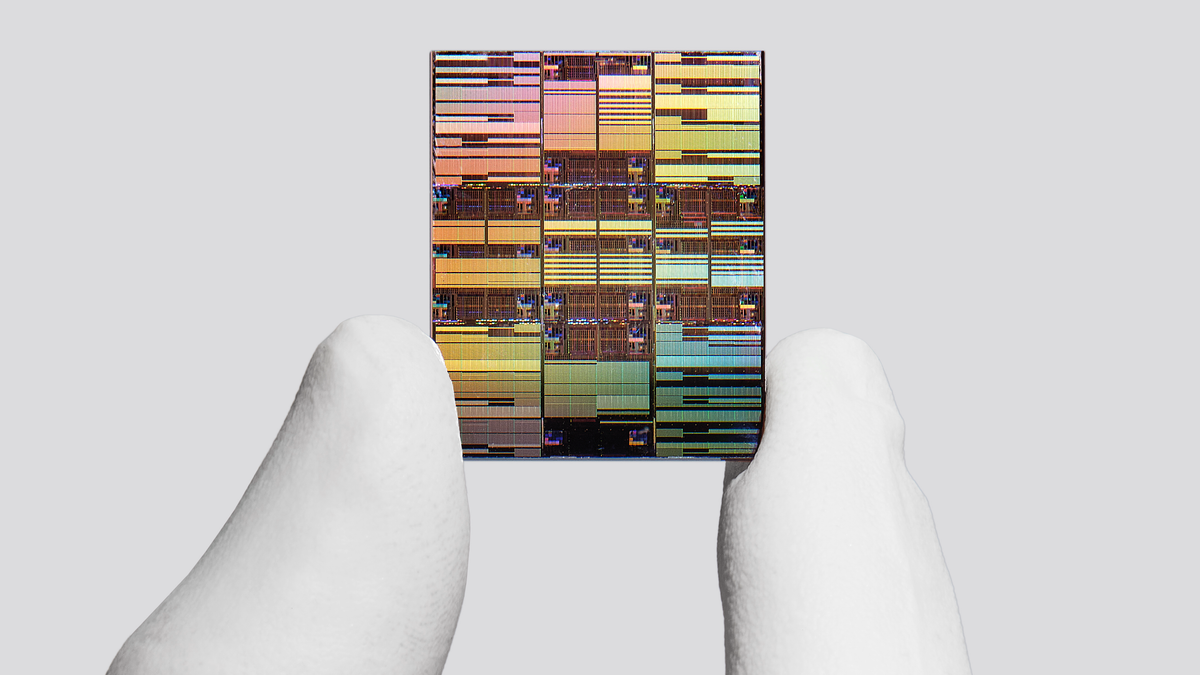 A microchip with intricate, colorful patterns is held between two fingers, illustrating semiconductor technology.