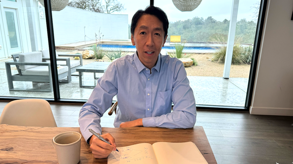 Andrew Ng is pictured writing in a notebook by a large window, with a garden and pool visible in the background.