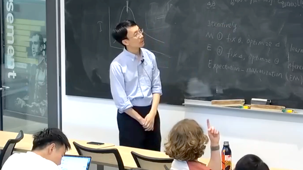Pengtao Xie is pictured standing near a chalkboard filled with mathematical notes, addressing a classroom of attentive students.